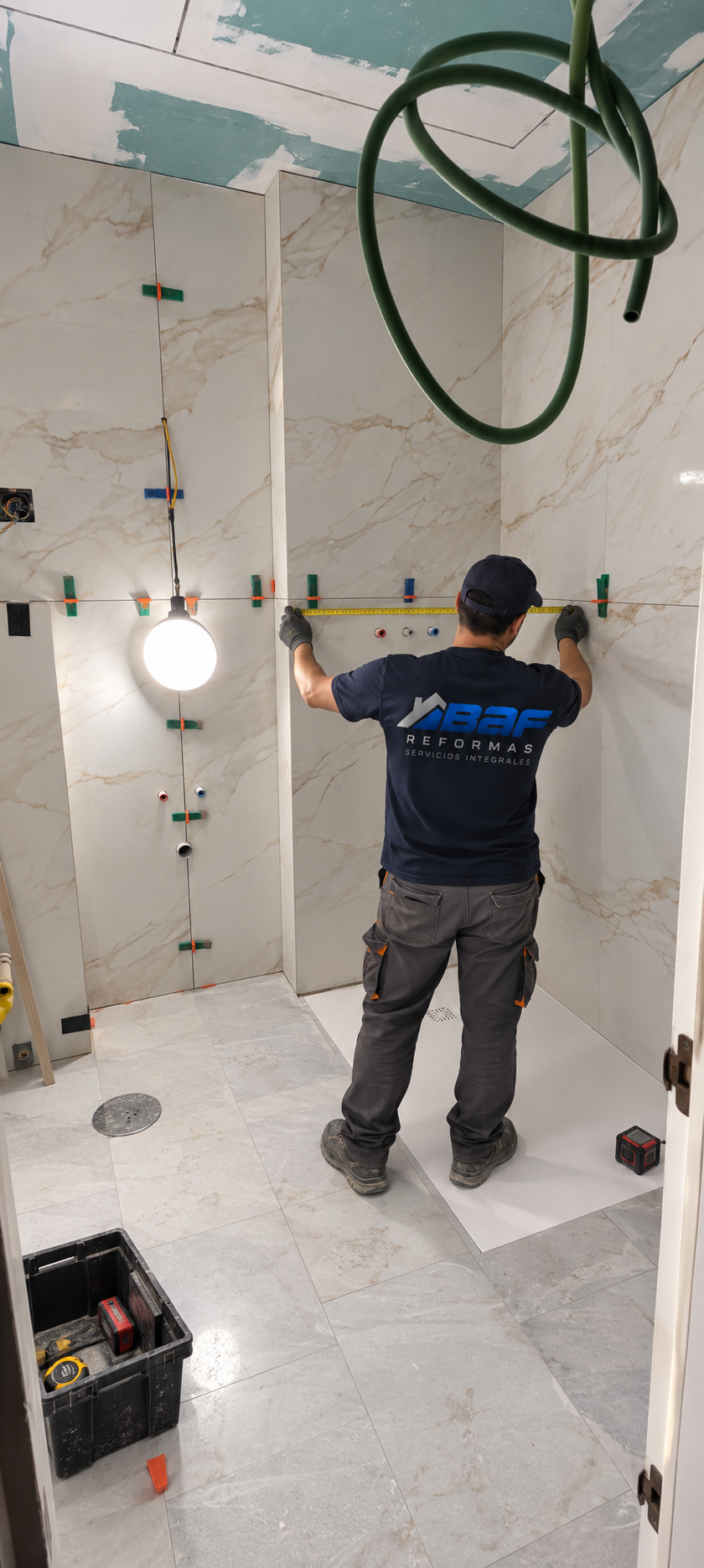 Técnico de BAF Reformas midiendo la pared durante el alicatado con revestimiento efecto mármol en un baño en reforma